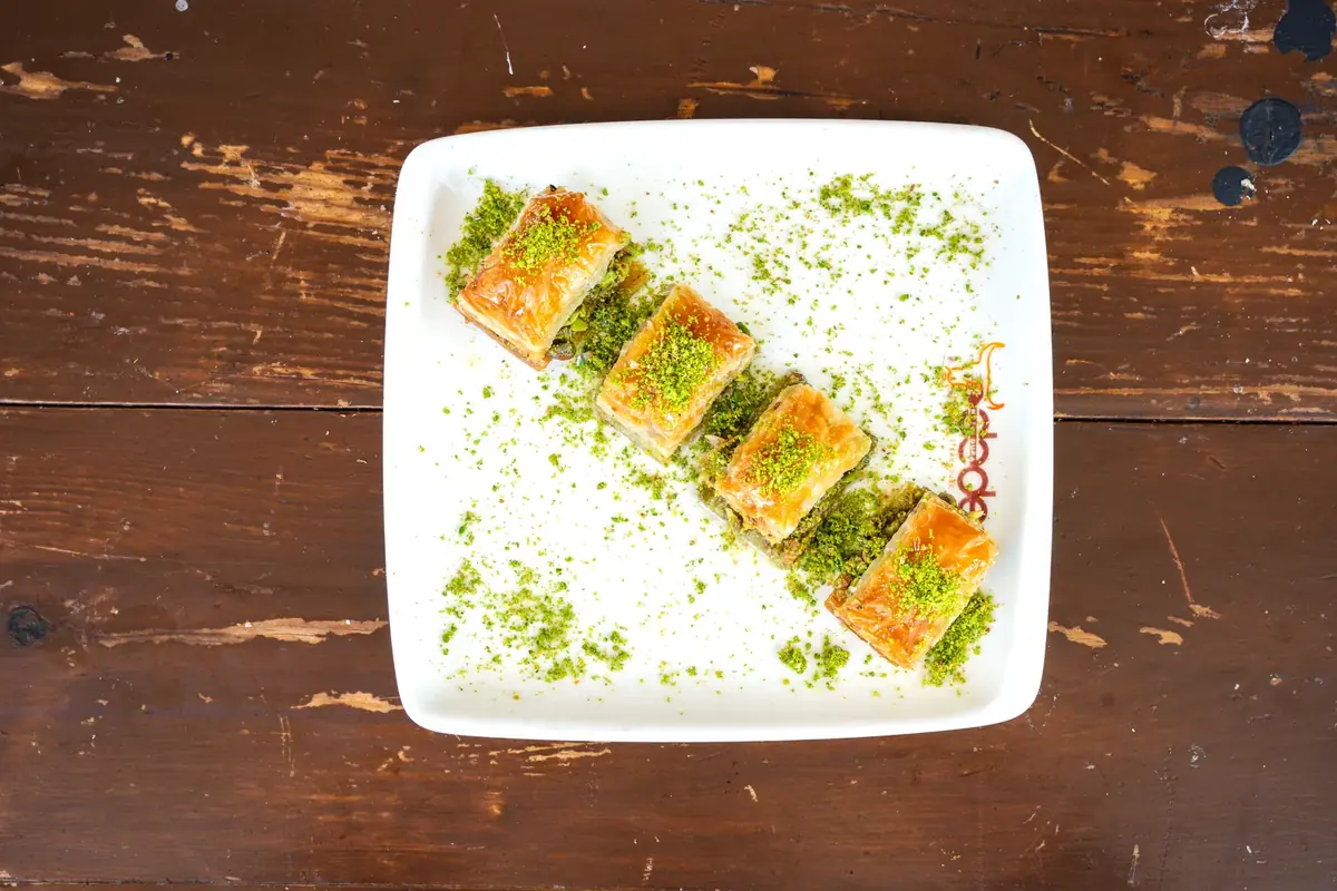 Dede Kebap'ta klasik fıstıklı baklava: logolu tabakta &ccedil;apraz dizilmiş kare dilimler