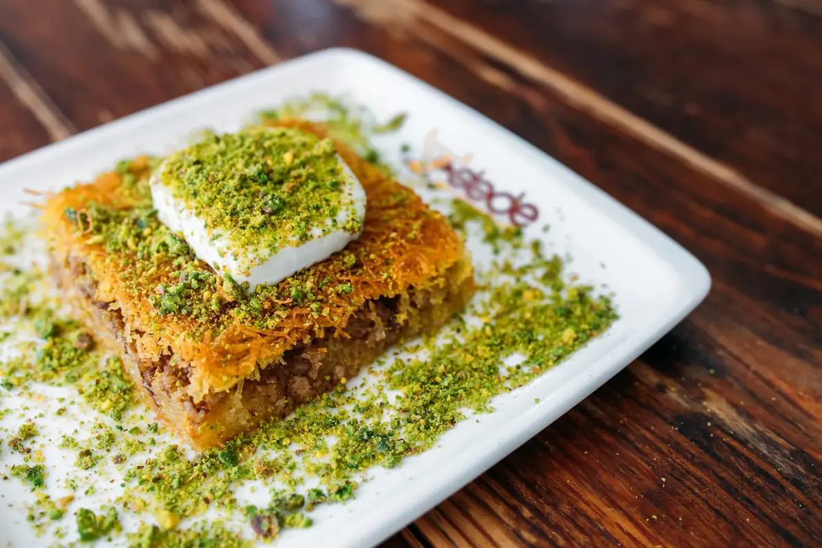 Dede Kebap'ta kaymaklı kadayıf: &uuml;zerinde kaymak ve toz Antep fıstığı olan tel kadayıf dilimi