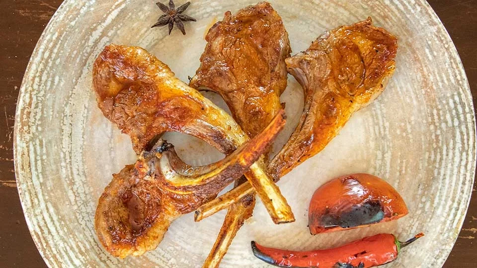 Kömür ateşinde ızgara edilmiş kuzu pirzola, yanında közlenmiş domates ve biber ile porsiyon sunum – Adana Dede Kebap Steak Burger Tatlı Kasap